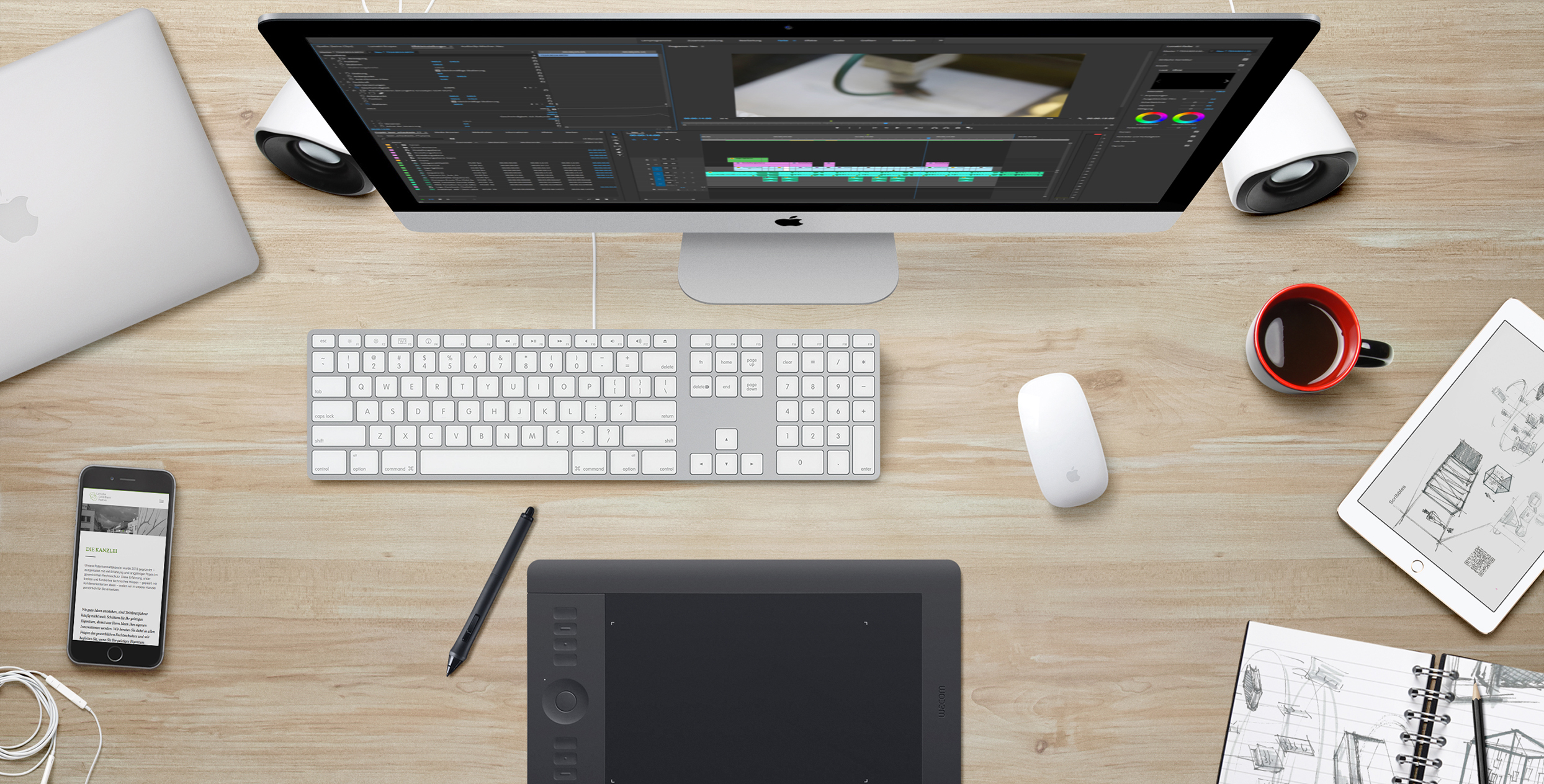 Ein Schreibtisch, der von Oben aufgenommen wurde. Man sieht einen iMac Computer, und ein Grafiktablet mit Stift