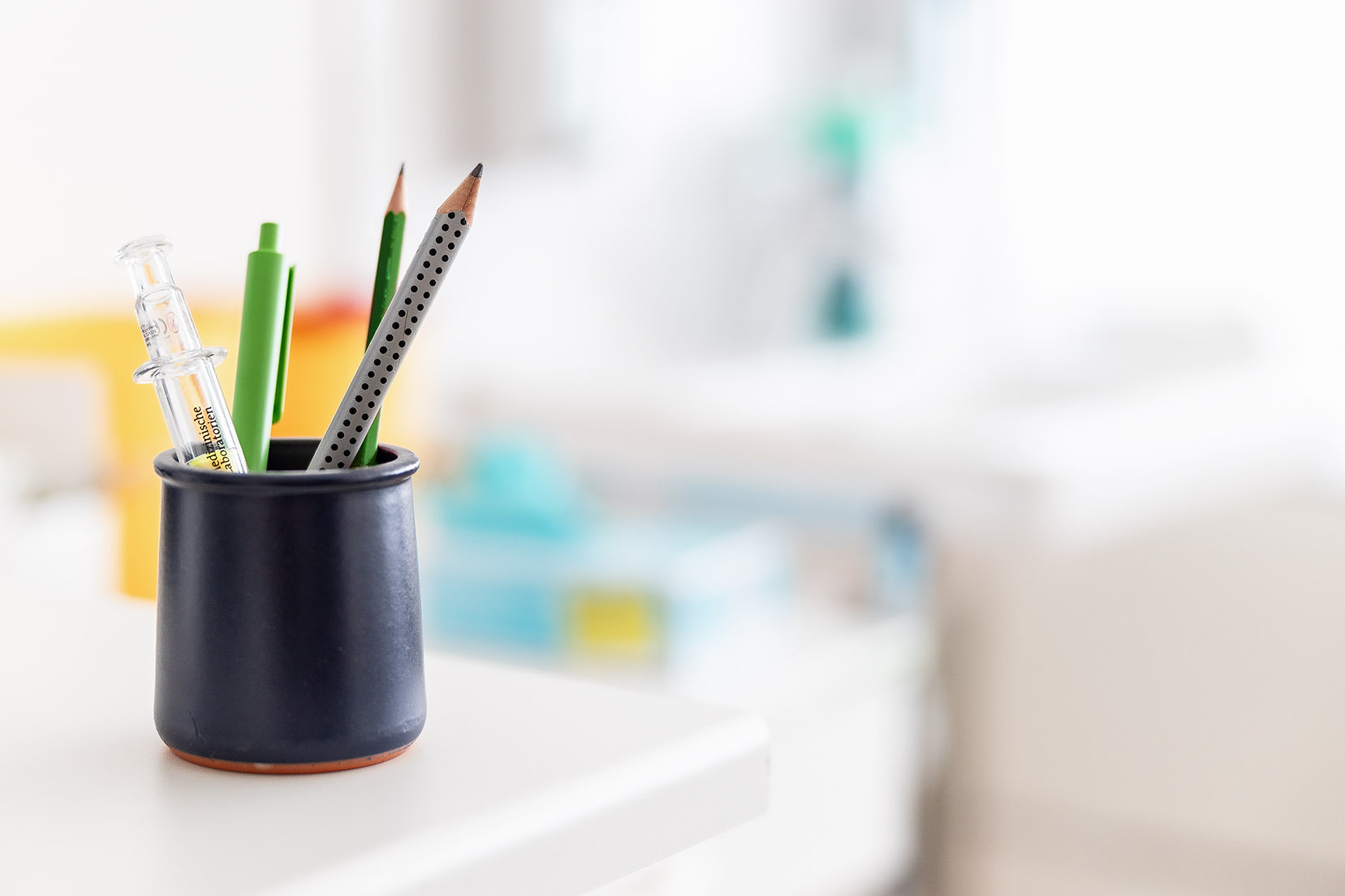 Stimmungsbild, das einen Becher mit Stiften auf einem Tisch zeigt, der Hintergrund ist unscharf.