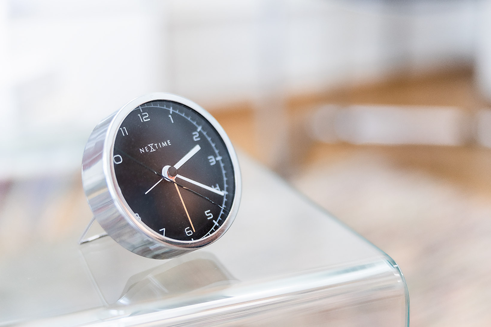 Ein Stimmungsbild, das eine Uhr auf einem Glastisch zeigt. Der Hintergrund ist unscharf.