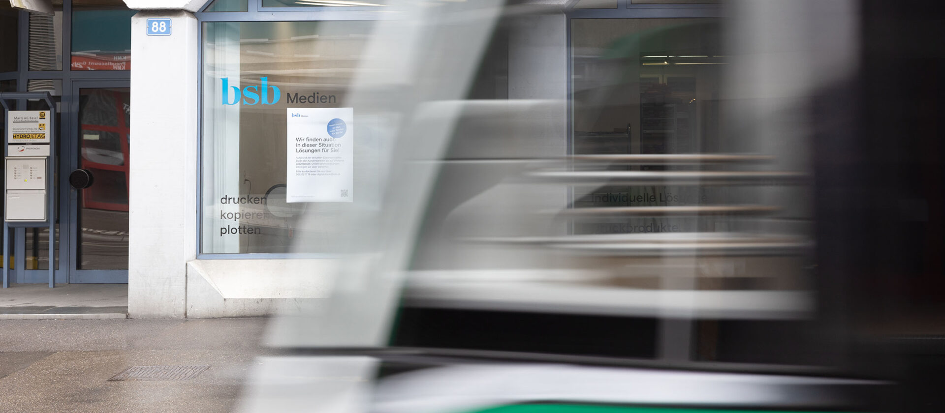 Im Hintergrund sieht man scharf den Druckladen vom BSB, im Vordergrund fährt unscharf ein Bus vorbei